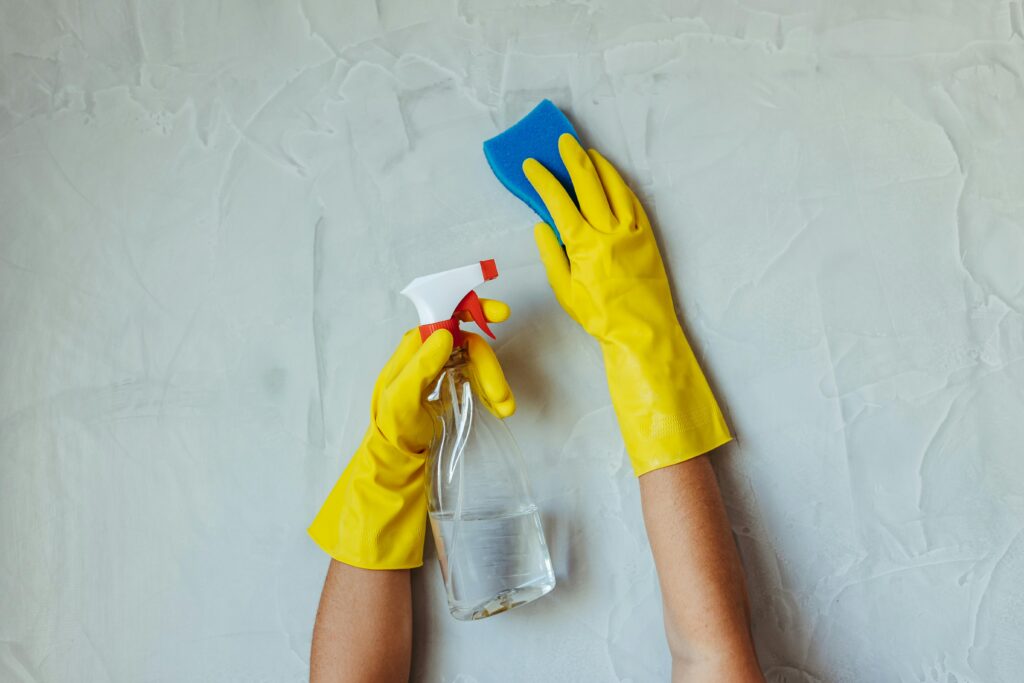 pexels photo 28576631 28576631 Close-up of hands in yellow gloves cleaning a wall with a spray bottle and sponge.