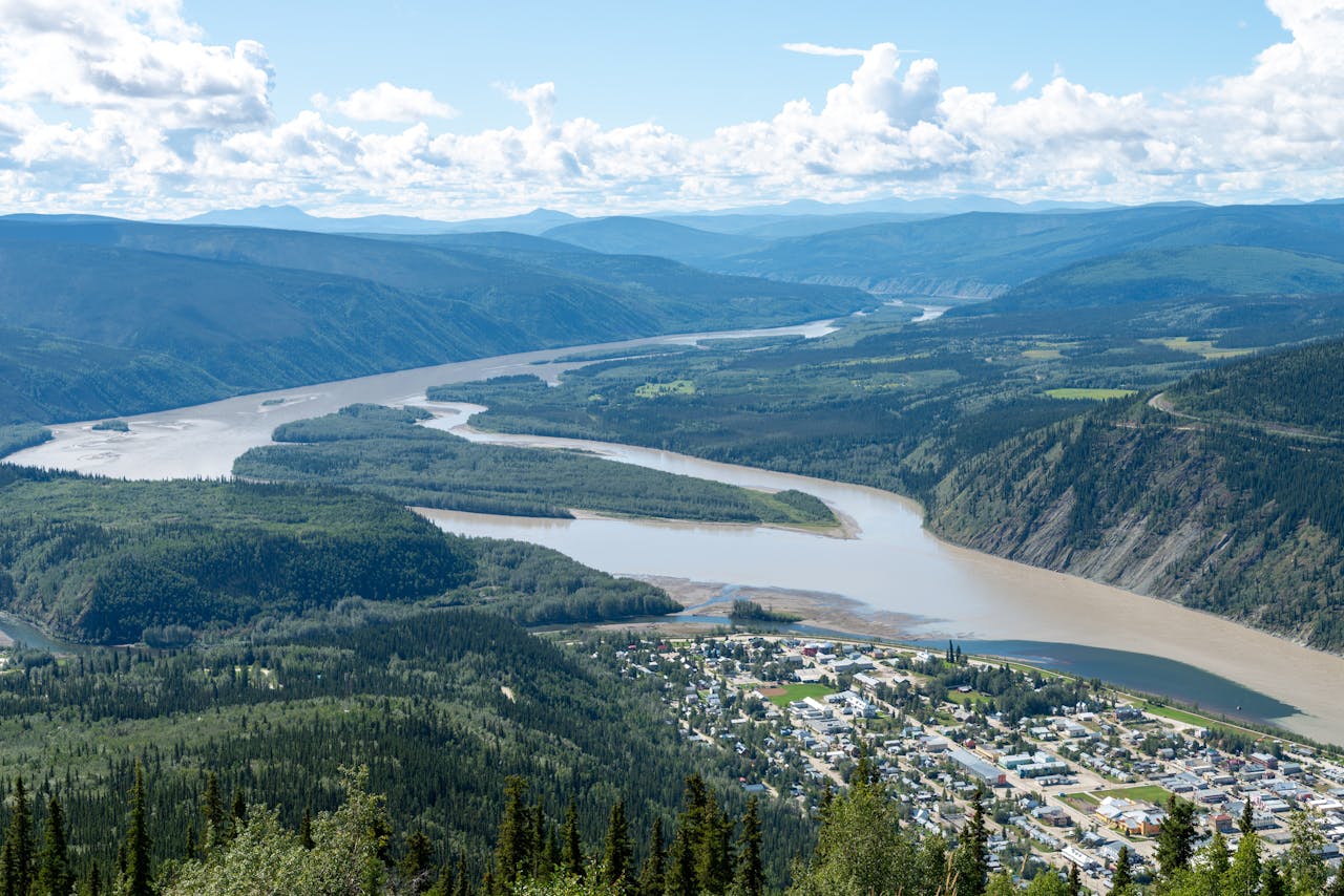 gallery-3 A breathtaking aerial shot of Dawson City, Yukon, Canada with the scenic Yukon River winding through lush green valleys.